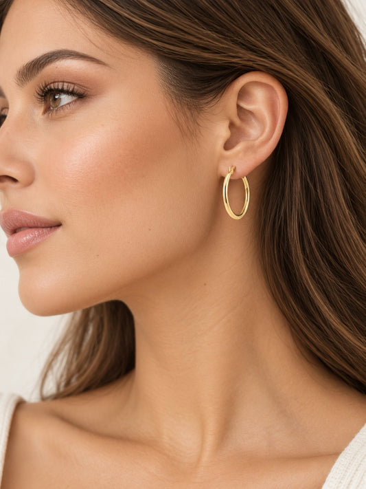 Thin gold-tone hoop earrings on model, small oval hoops
