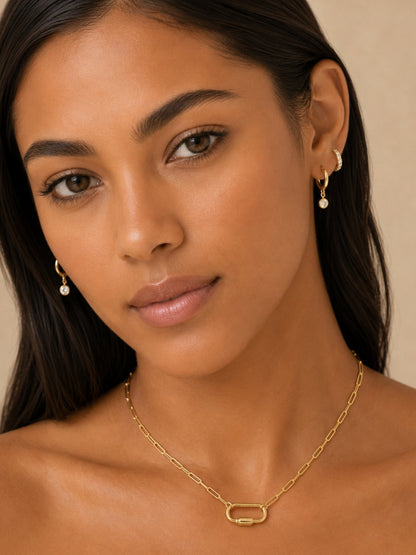 Gold diamond huggie hoops with round drop charms on model’s ear