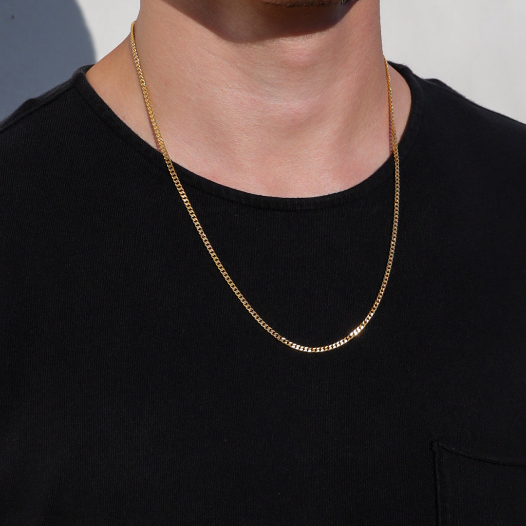 Gold Cuban link chain necklace with smooth links, worn at the collar on a model.