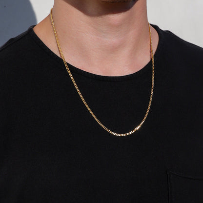 Gold Cuban link chain necklace with smooth links, worn at the collar on a model.