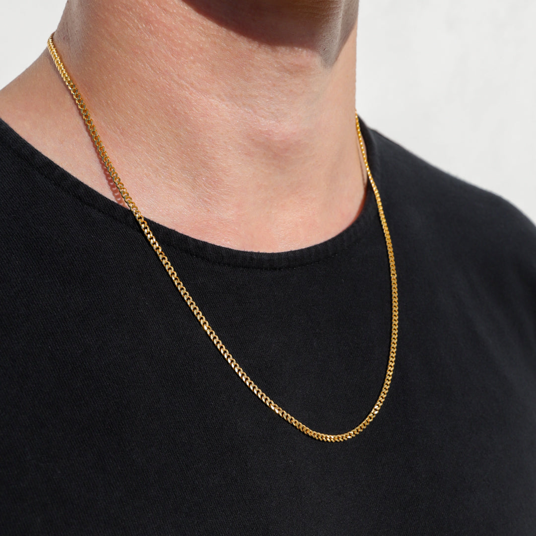 Gold Cuban link chain necklace layered on a model’s neck over a black shirt.