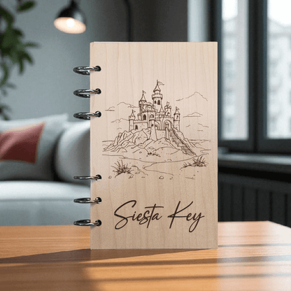 A6 refillable notebook on desk, light tan cover with black spiral rings, line-art castle and Siesta Key