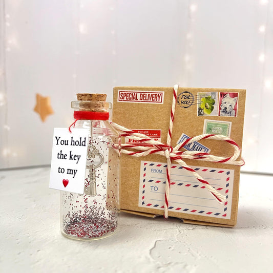 Miniature glass message bottle with key note and glitter, beside craft gift box