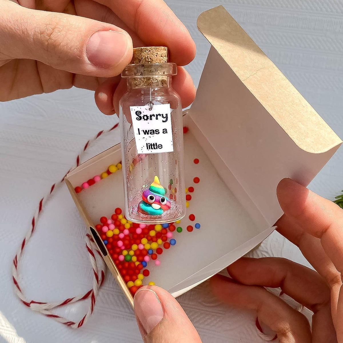 Glass apology message bottle with cork and printed label held above an open gift box