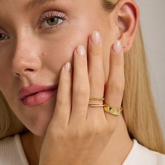 Gold ribbed band ring on finger, shown with stacked jewelry.