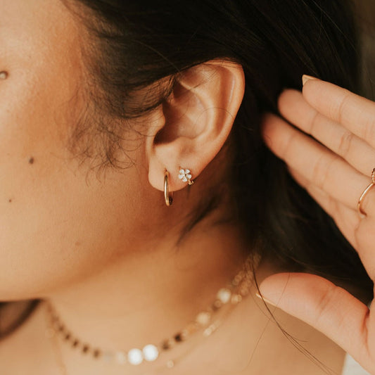 Gold flower mini hoop earrings worn on an ear