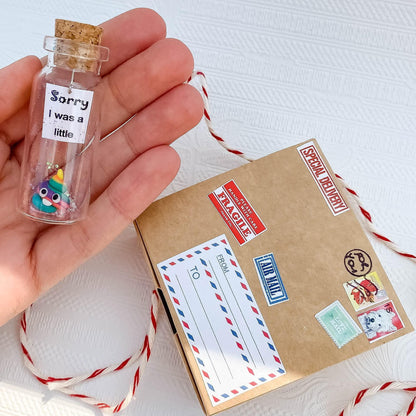 Glass apology message bottle with cork held above an open kraft gift box and note