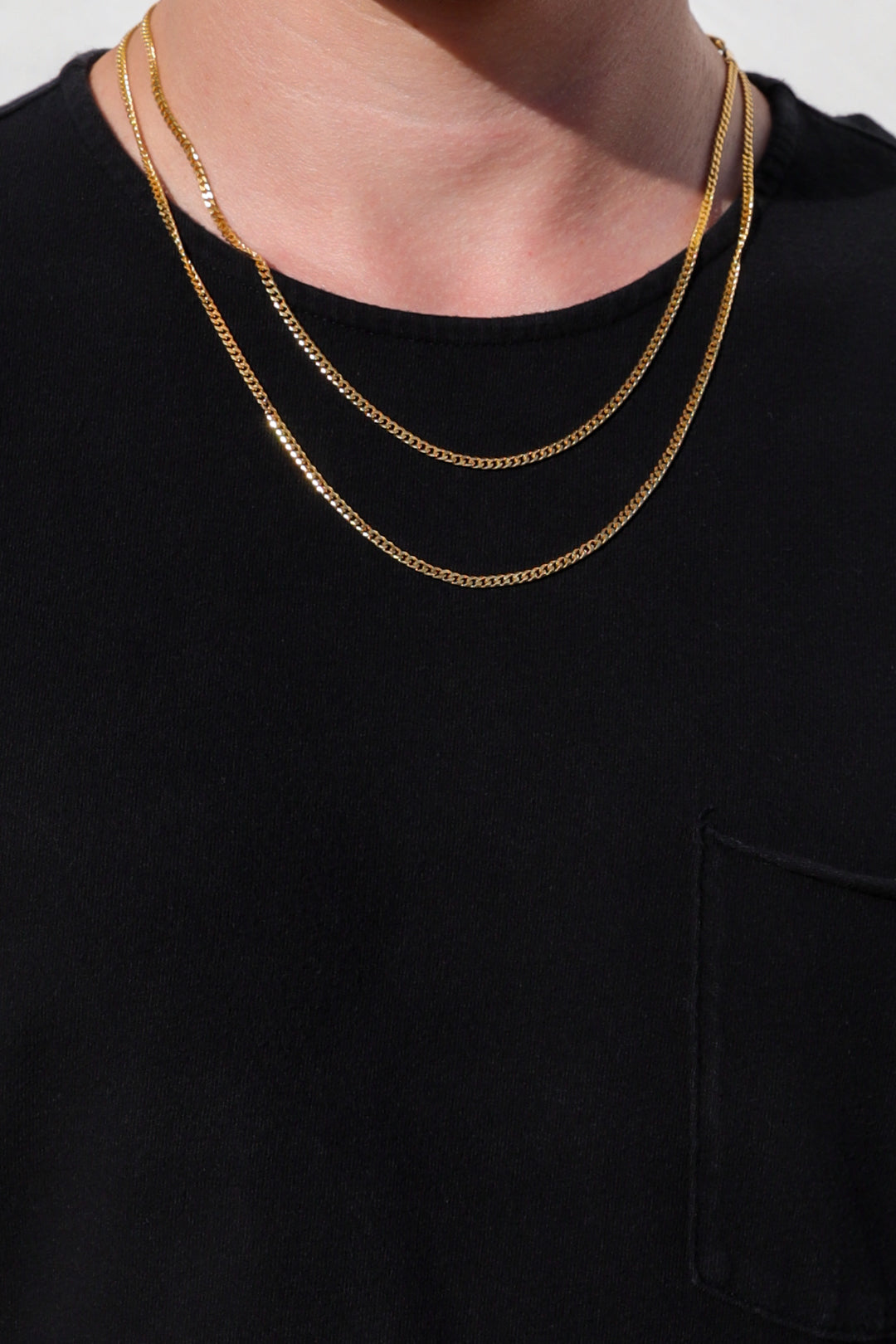 Gold Cuban link chain necklace layered on a model, resting on the chest.