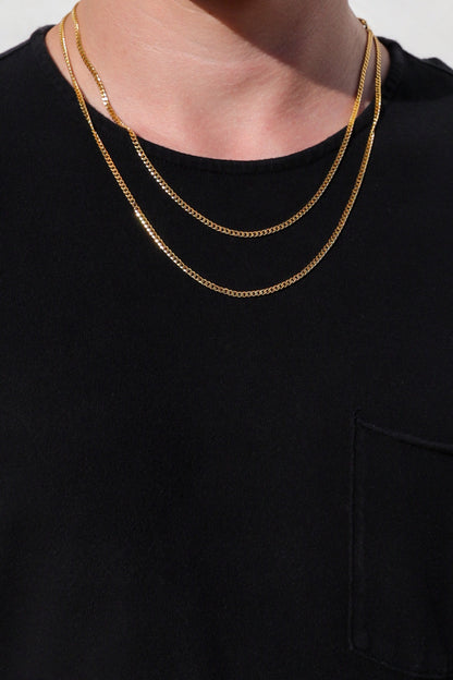 Gold Cuban link chain necklace layered on a model, resting on the chest.