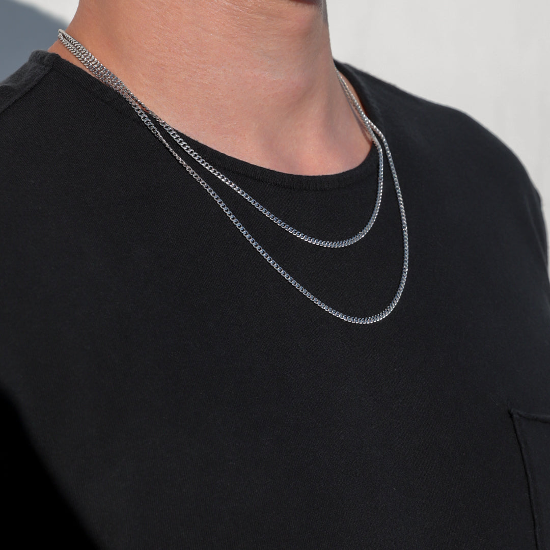 Layered silver-tone Miami Cuban link chain necklaces on the neck of a dark shirt