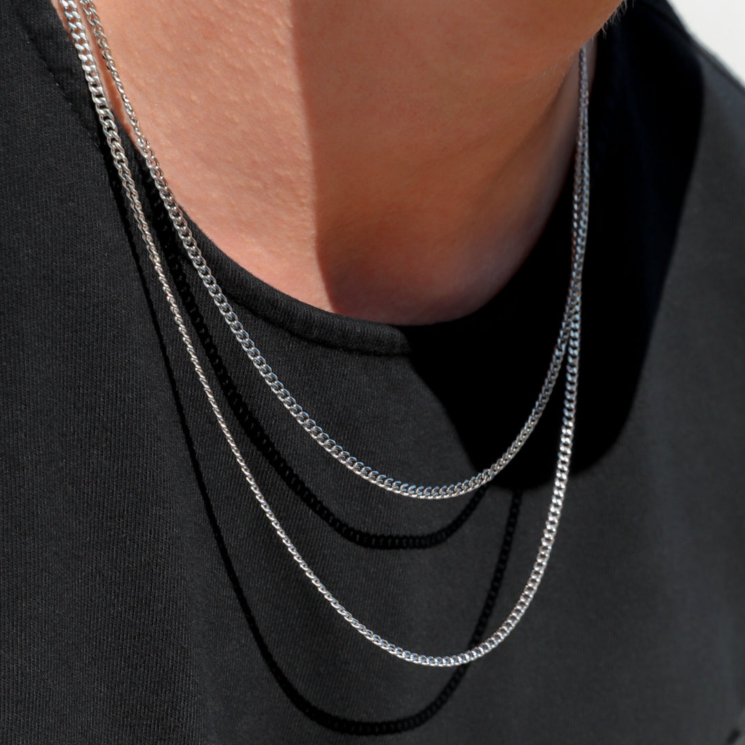 Silver Cuban link chain necklace layered on a model, close-up at the neckline.