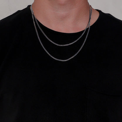 Silver Cuban link chain necklace layered on a model’s neck over a black shirt.