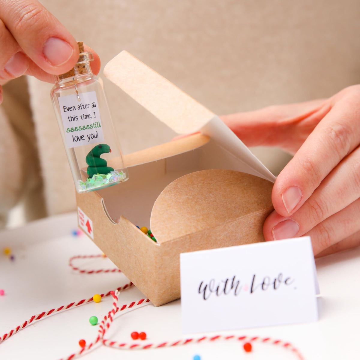 Hand placing a corked message bottle with 'With love' card in a kraft gift box