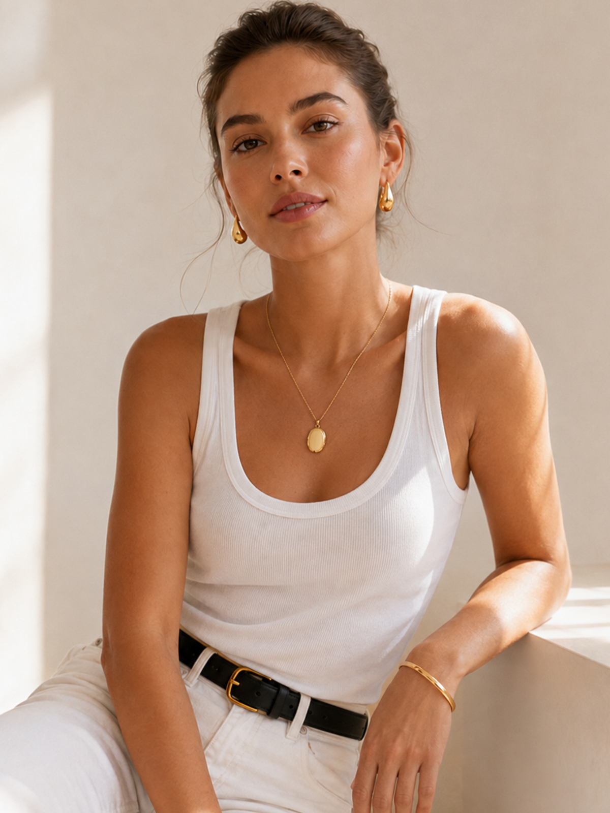 Gold oval locket necklace with round pendant face worn on white tank