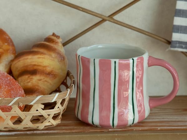 Striped ceramic mug with pink handle and vertical green lines, next to pastries on a tray