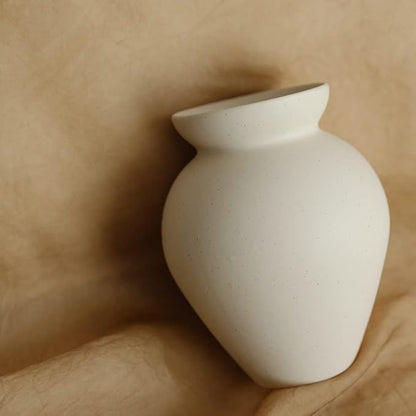 Close-up of cream ceramic milk can vase with matte speckled surface and flared rim.