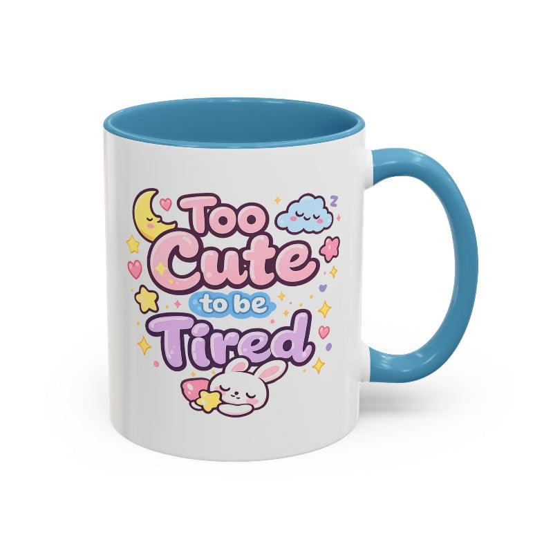 White mug with blue rim and handle, “Too Cute to be Tired” text and bunny.