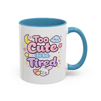 White mug with blue rim and handle, “Too Cute to be Tired” text and bunny.