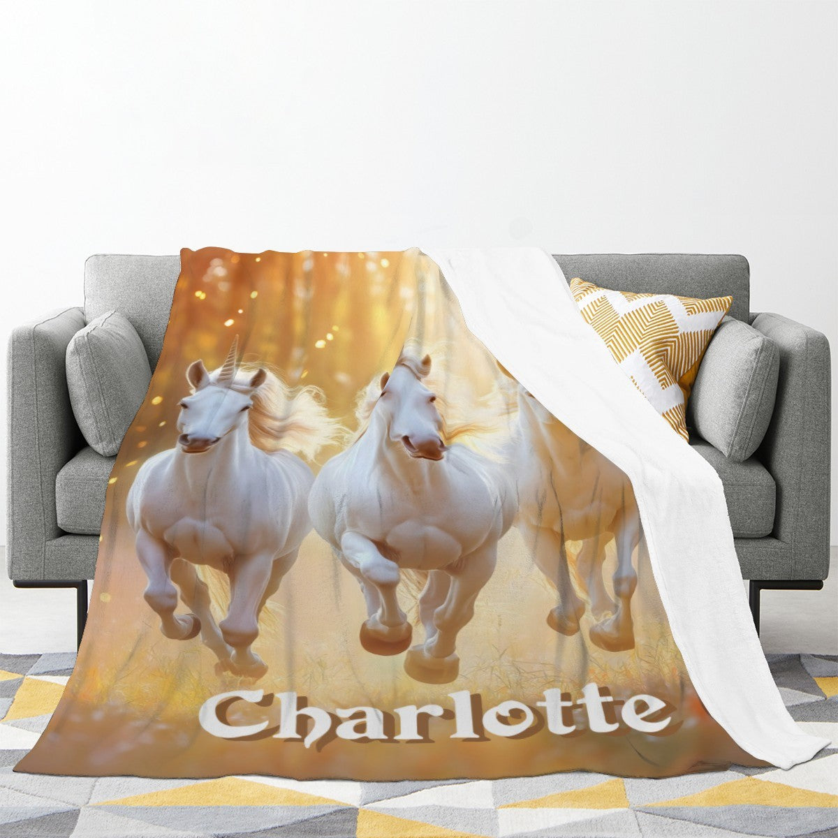 Unicorn name blanket on sofa with three white horses and gold sparkle, name Charlotte