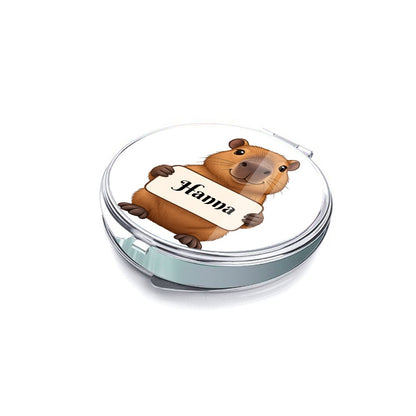 Side view of a round silver compact mirror with capybara cover art