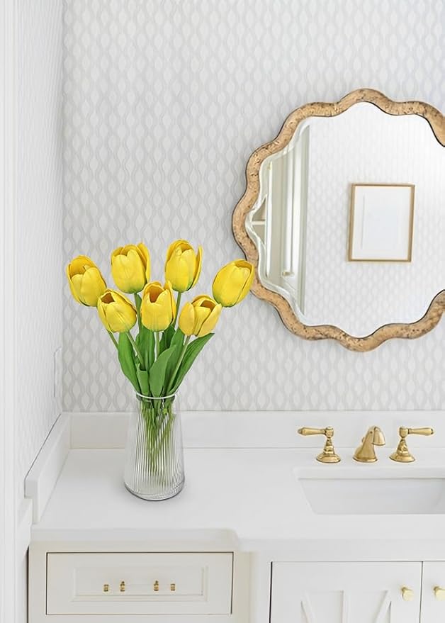 Yellow faux tulip stems in a clear vase beside a wall mirror