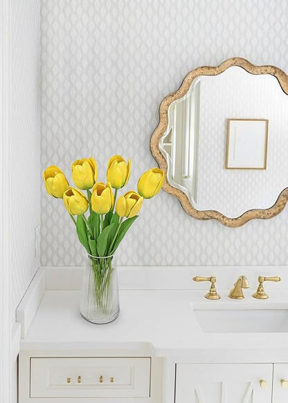 Yellow faux tulip stems in a clear vase beside a wall mirror