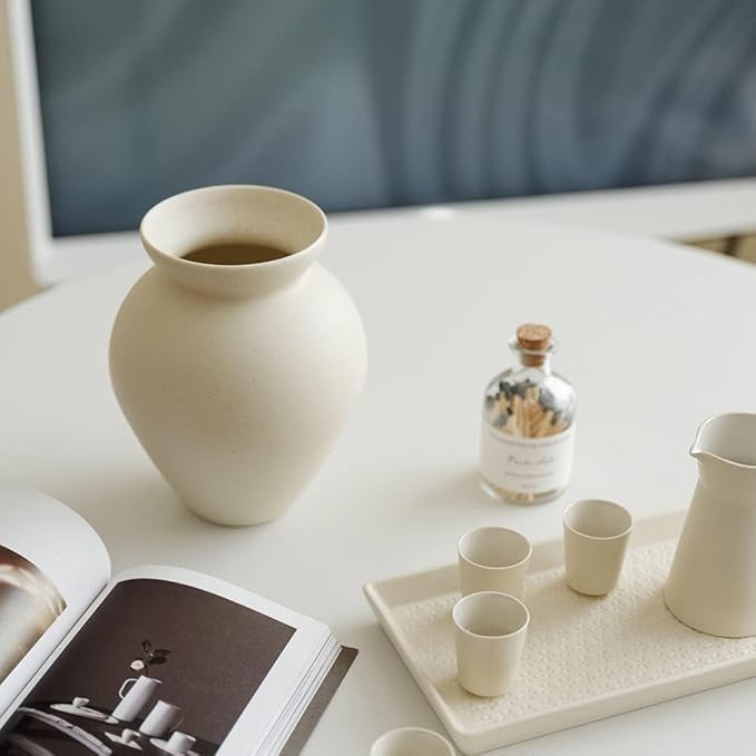 Cream ceramic milk can vase with matte speckled finish, placed on a tabletop setting.