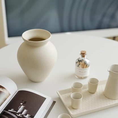 Cream ceramic milk can vase with matte speckled finish, placed on a tabletop setting.