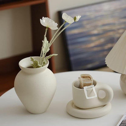 Cream ceramic milk can vase with matte speckled finish holding white flowers.