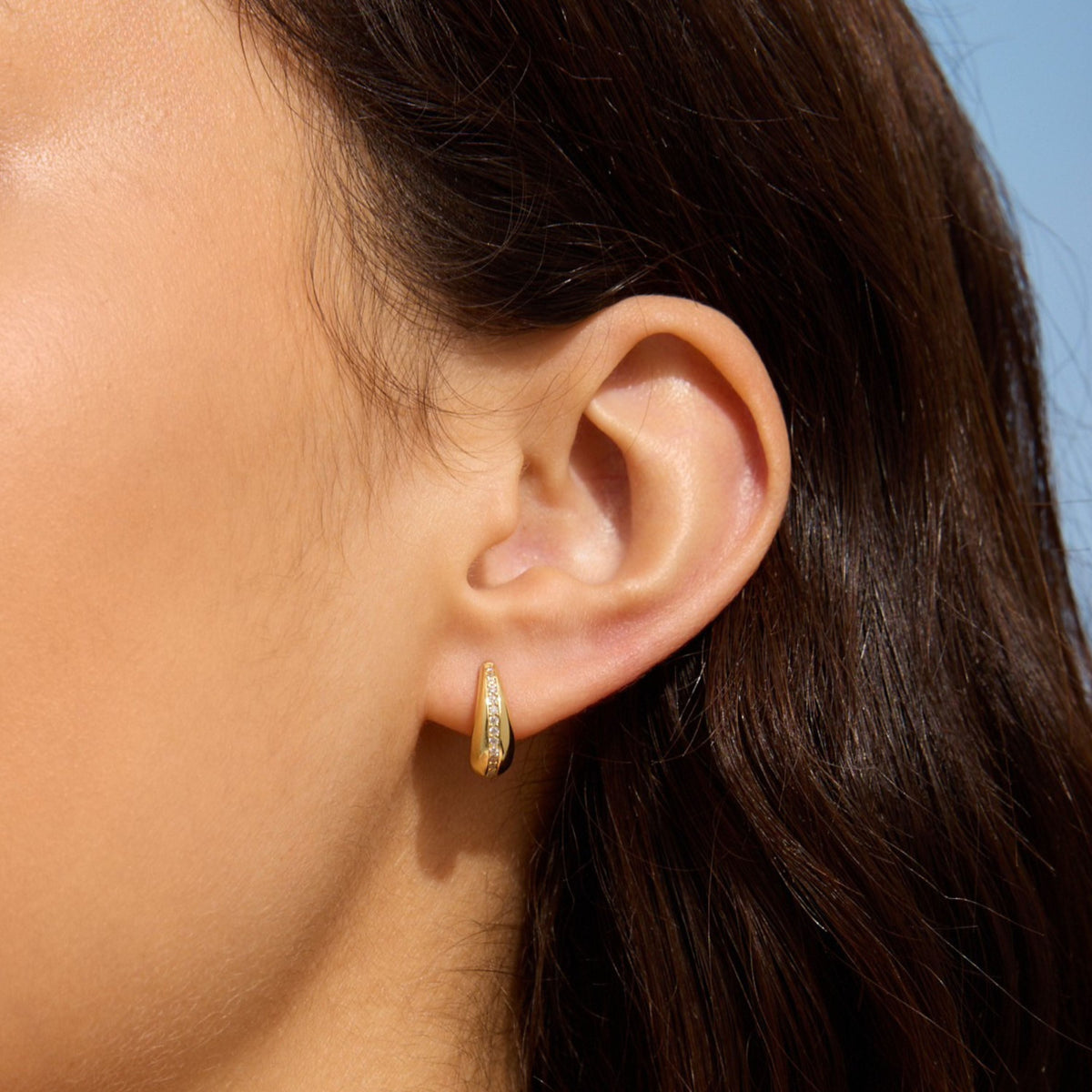 Teardrop diamond huggie earring in gold, shown on the ear