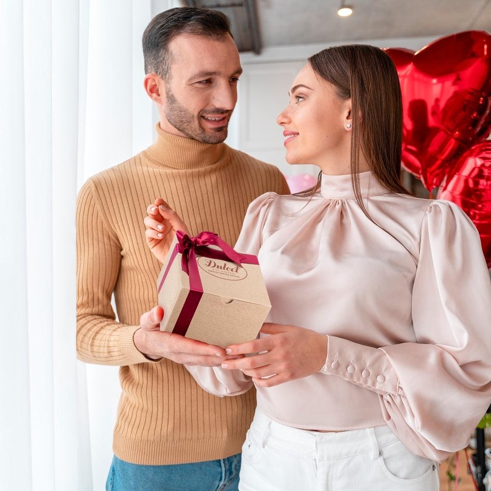 Gift box with red ribbon held by two people in matching satin bow wrap