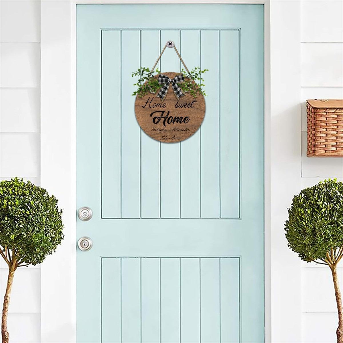 Round wooden “Home Sweet Home” hanging sign with plaid bow and green foliage, names