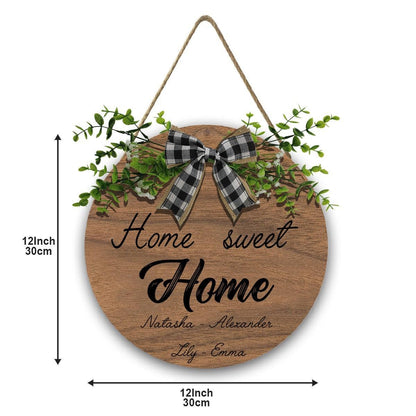 Round wooden “Home Sweet Home” sign with plaid bow, green foliage, and rope hanger