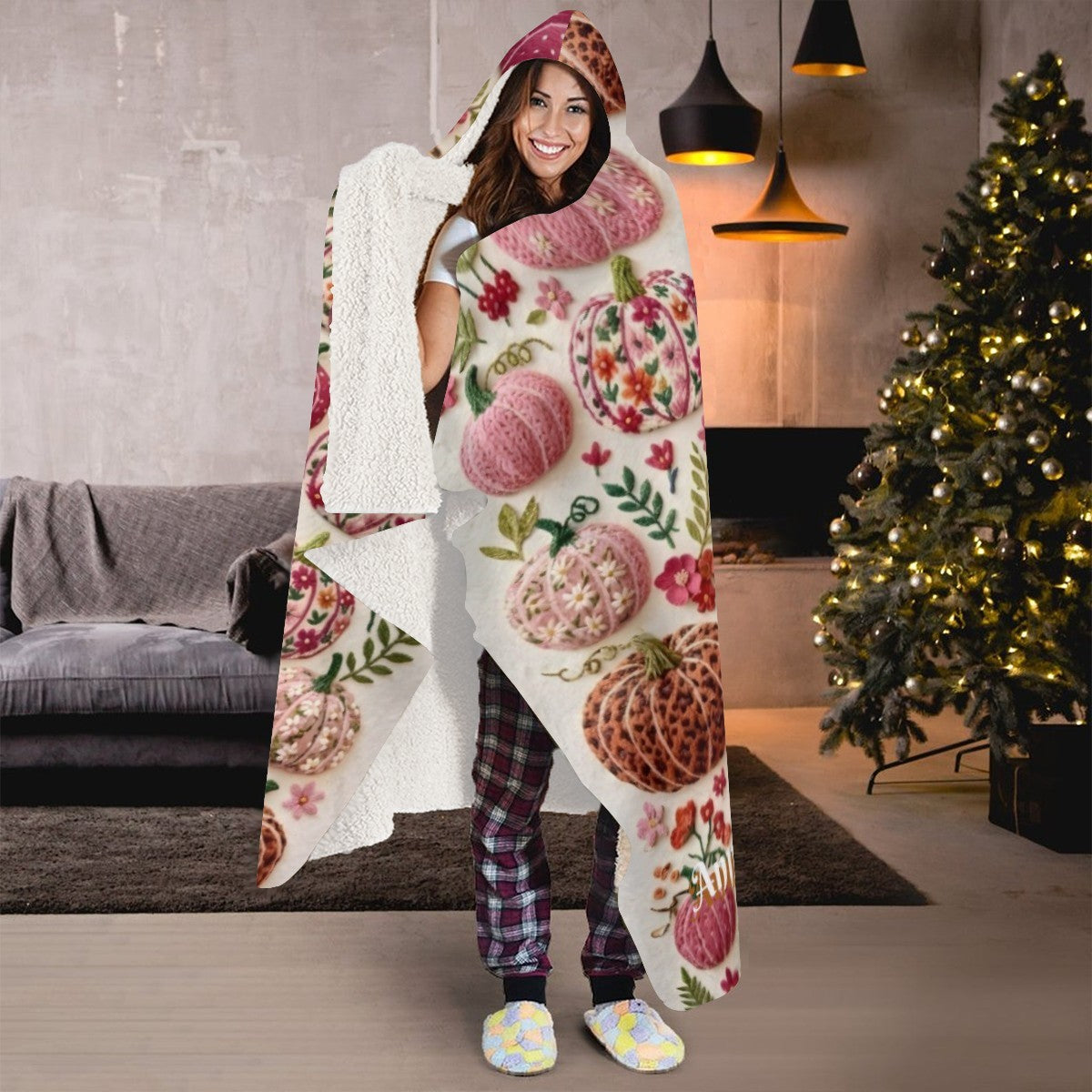 Sherpa-trimmed hooded blanket with pumpkin print, worn over plaid pajama pants.