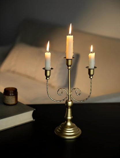 Gold metal three-stem taper candle holder with curled vine arms and three lit candles
