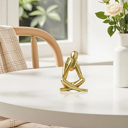 Gold reading thinker bookend statue on tabletop, seated with arms resting on knees.