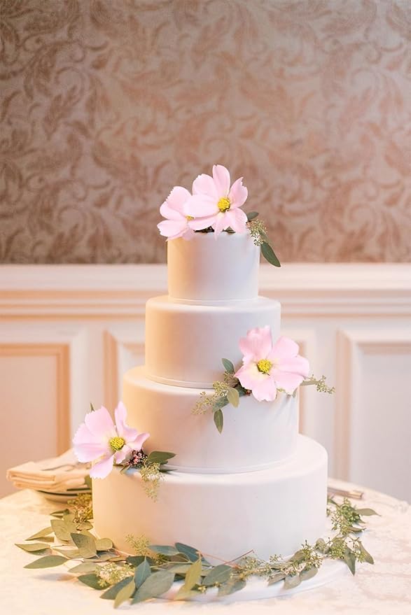 Light pink faux daisy-style flower stems with green leaves on white cake tiers