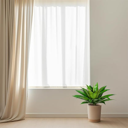 Artificial green agave plant in white pot with spiky green leaves near window