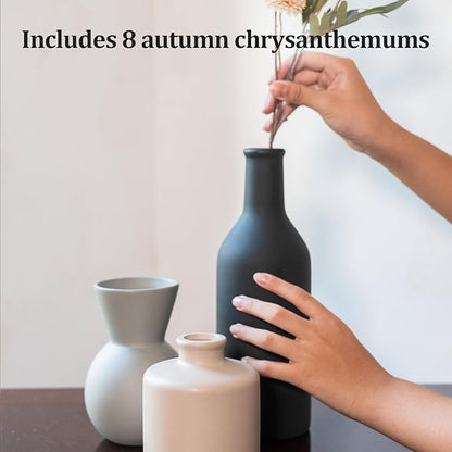 Ceramic vase with faux chrysanthemum stems in black, alongside gray and cream vases