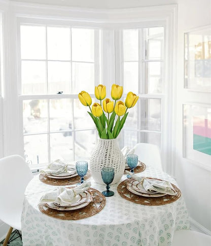Yellow faux tulip stems in a clear glass vase on a dining table