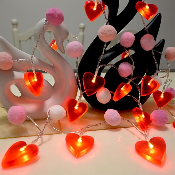Valentine LED string lights with red heart bulbs and pink pom poms, lit up