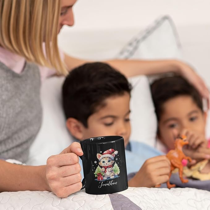 Black mug with kitten holiday print and 'Jonathan' on a quilted bed scene.