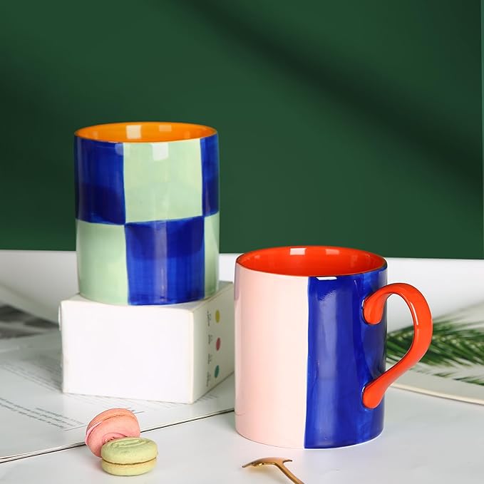 Two glazed ceramic mugs: blue-mint checkered with orange handle and red-blue with orange handle