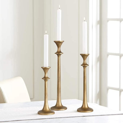 Brass taper candle holders holding three lit candles, staggered heights.