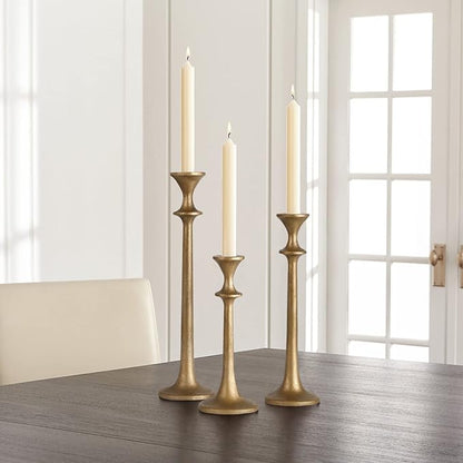 Brass iron taper candle holders holding three cream taper candles on table.