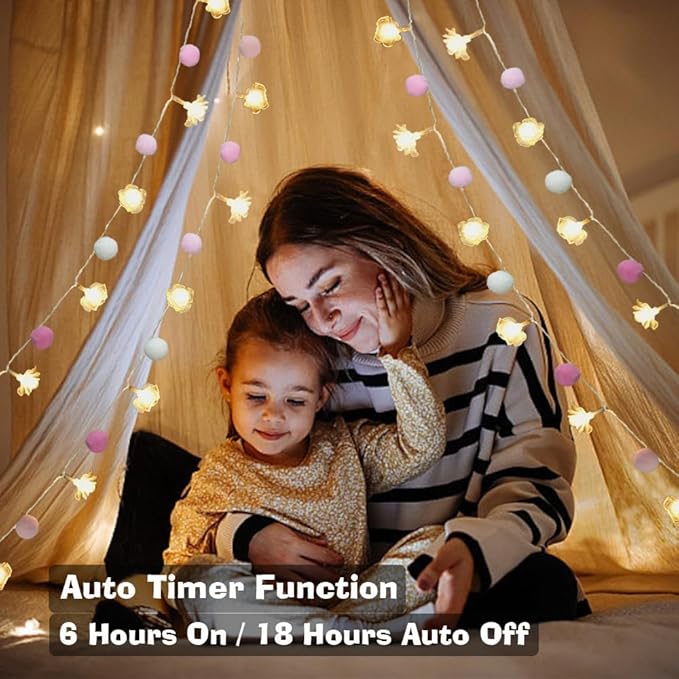 Pink and white pom-pom fairy lights with warm rose LED bulbs draped on a canopy