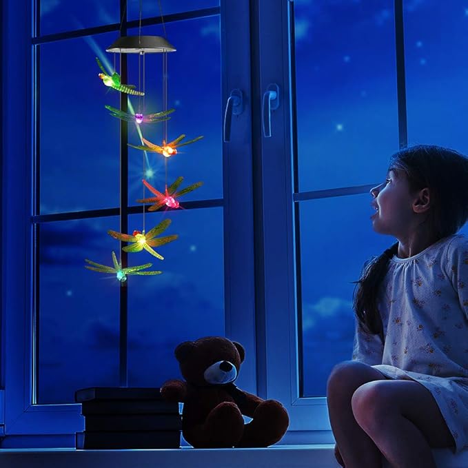 Solar wind chimes with glowing dragonfly charms hanging near a blue window at night
