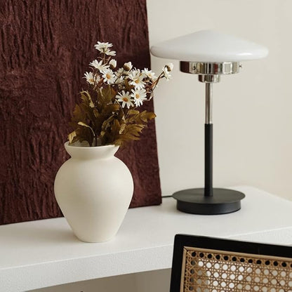 Cream ceramic milk can vase holding a small bouquet of white flowers on a table.