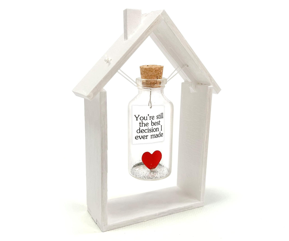 Heart message bottle in white wooden house frame, corked glass bottle with red heart