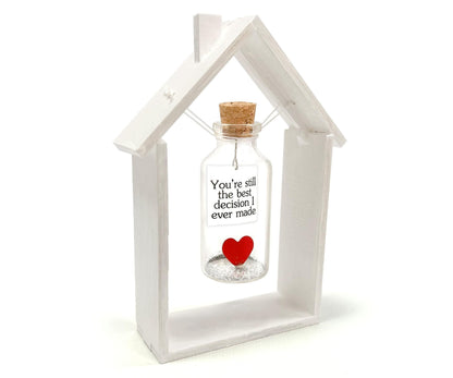 Heart message bottle in white wooden house frame, corked glass bottle with red heart